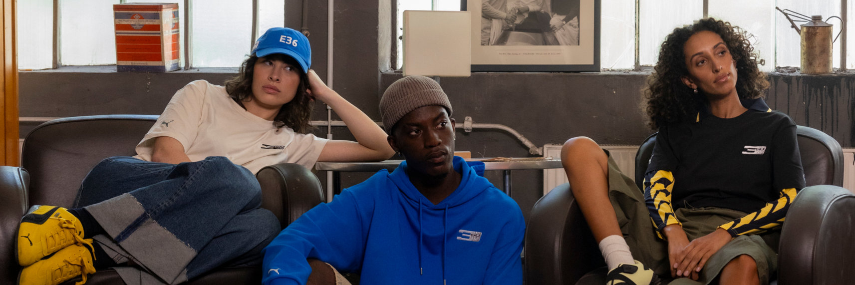 A man and two women wearing BMW apparel lounge on chairs in a small room.