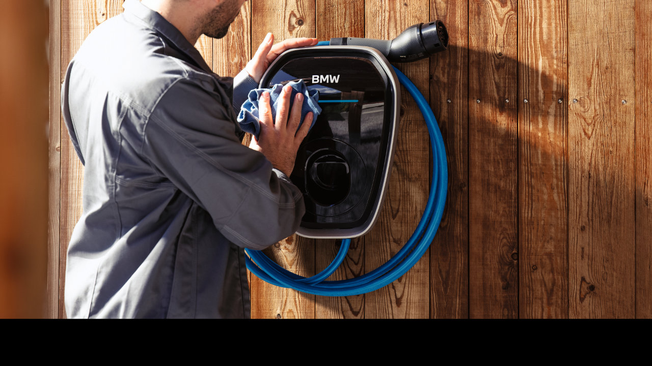 A man wipes down a BMW Wallbox charger that is mounted to a wood-paneled wall.