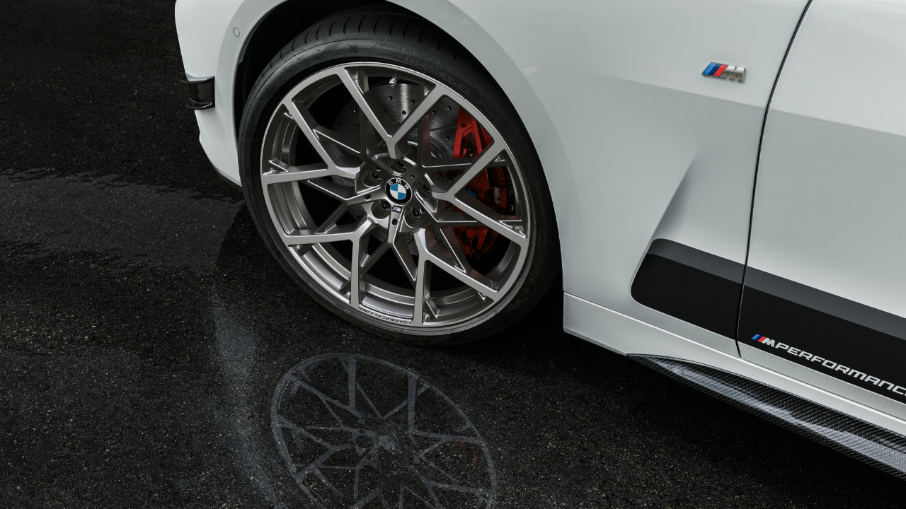 The left front wheel and tire of a white BMW M model.