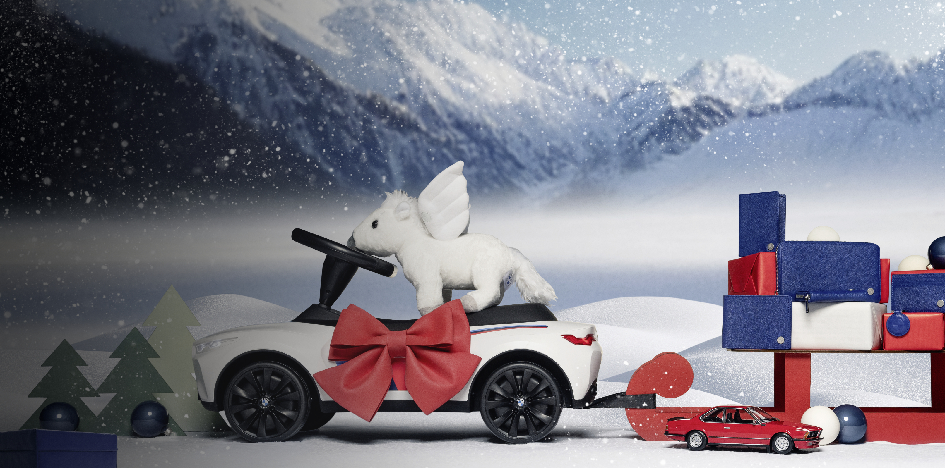 A BMW toy car with a plush Pegasus and a red bow tows a sled of gifts and toys on a snowscape